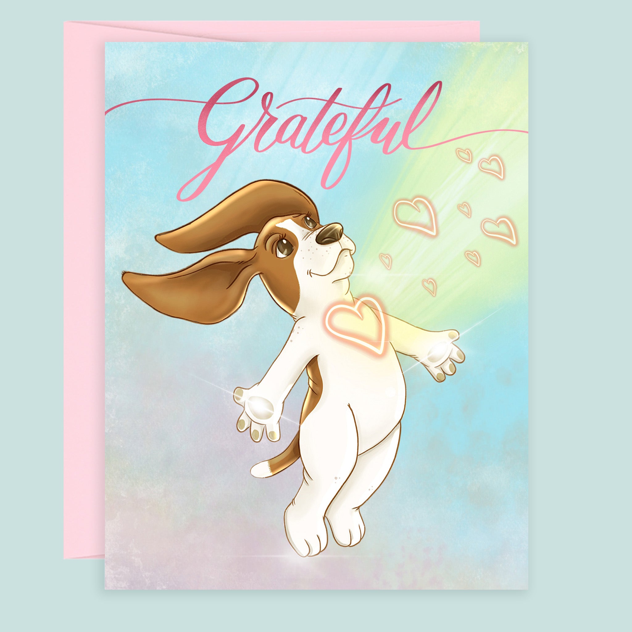 A thank you note card featuring an illustration of a brown and white basset hound radiating with glowing hearts, under the word 'Grateful' in pink hand drawn script. A pink envelope is partially visible behind the card against a pale blue background.