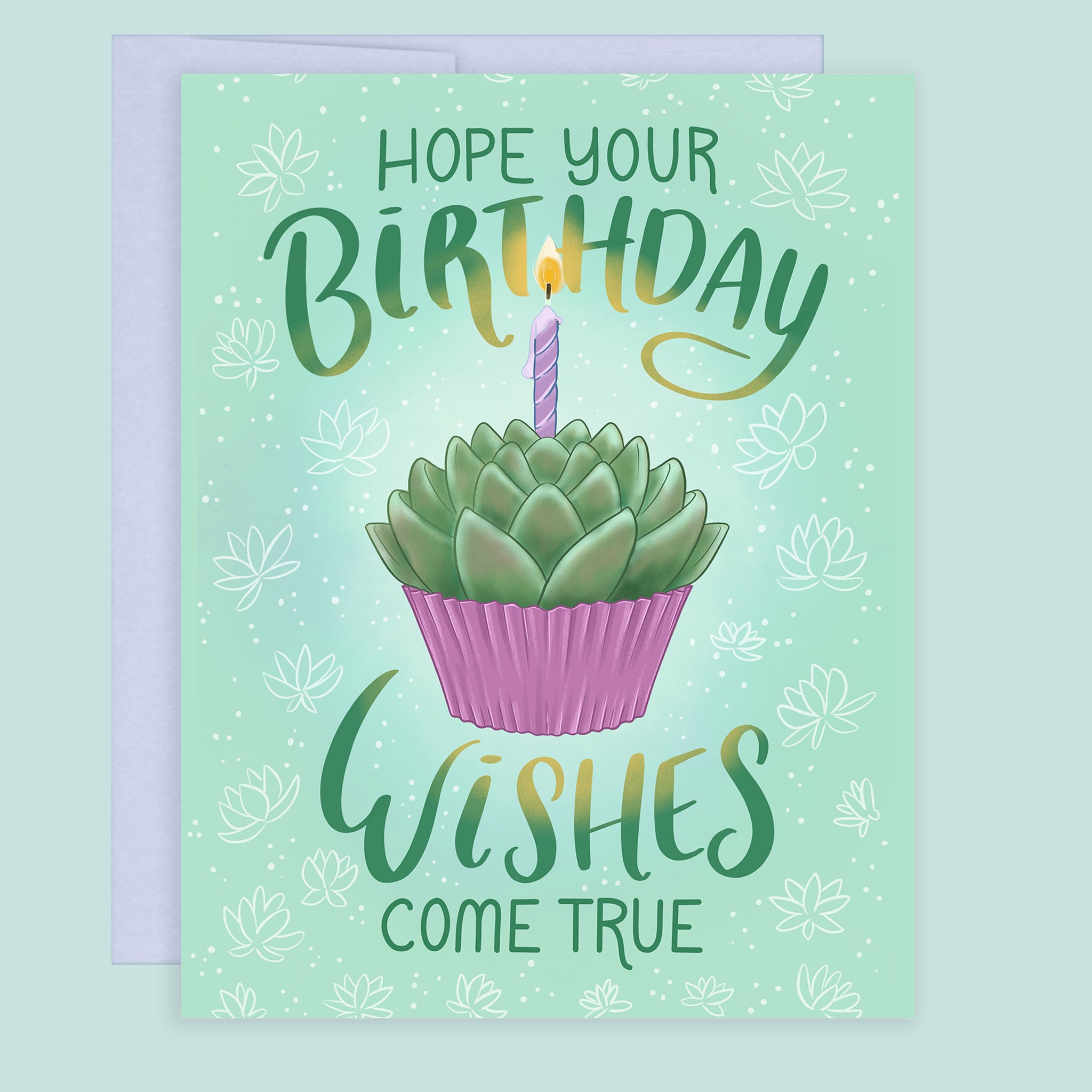 A birthday greeting card with a coordinating purple envelope. The card features a soft green background with white succulent floral motifs, a central illustration of a succulent in a pink cupcake with a lit purple candle, and the text 'HOPE YOUR BIRTHDAY WISHES COME TRUE' in green hand lettering.