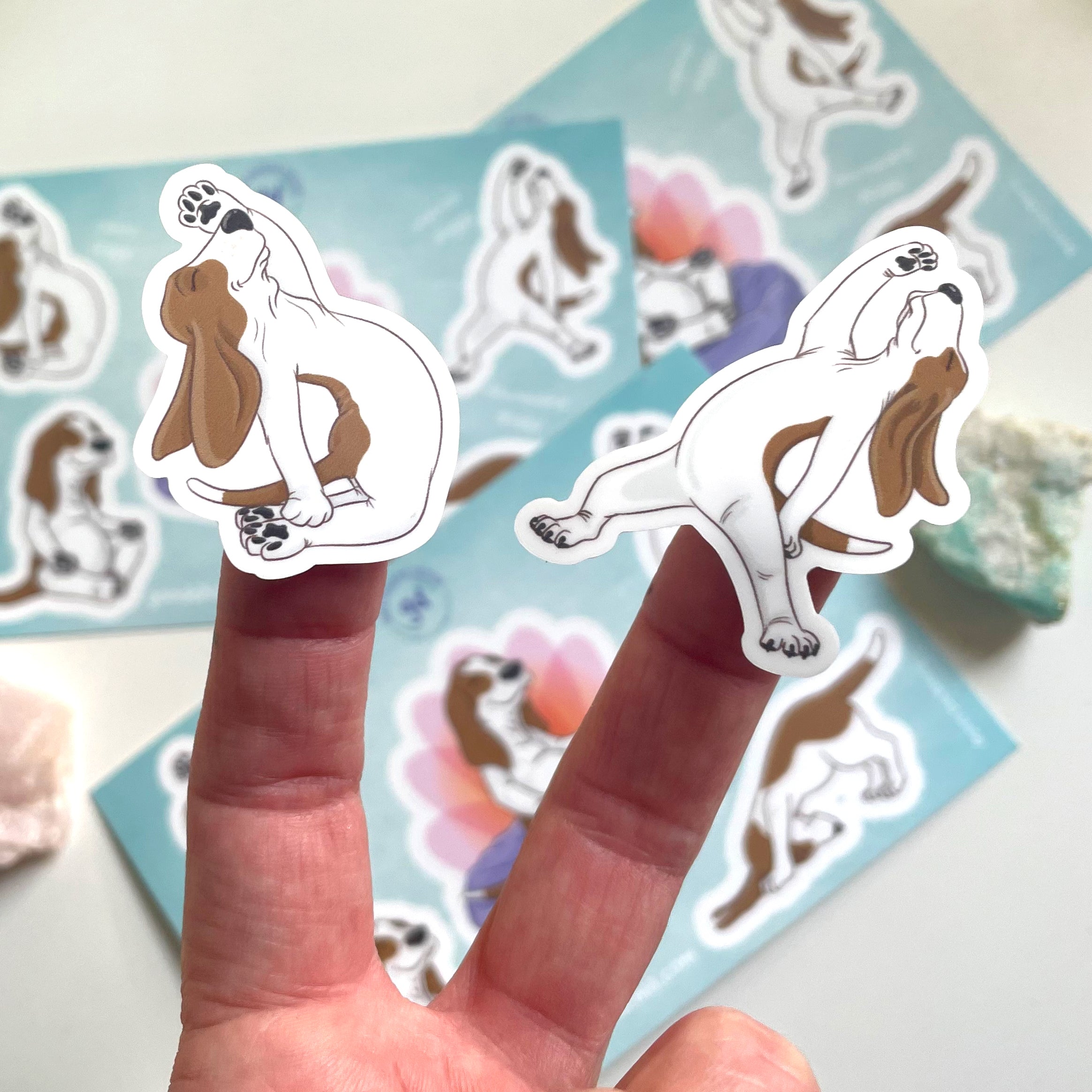 Hand holding a sticker of dogs in yoga poses with a blue background featuring more stickers.