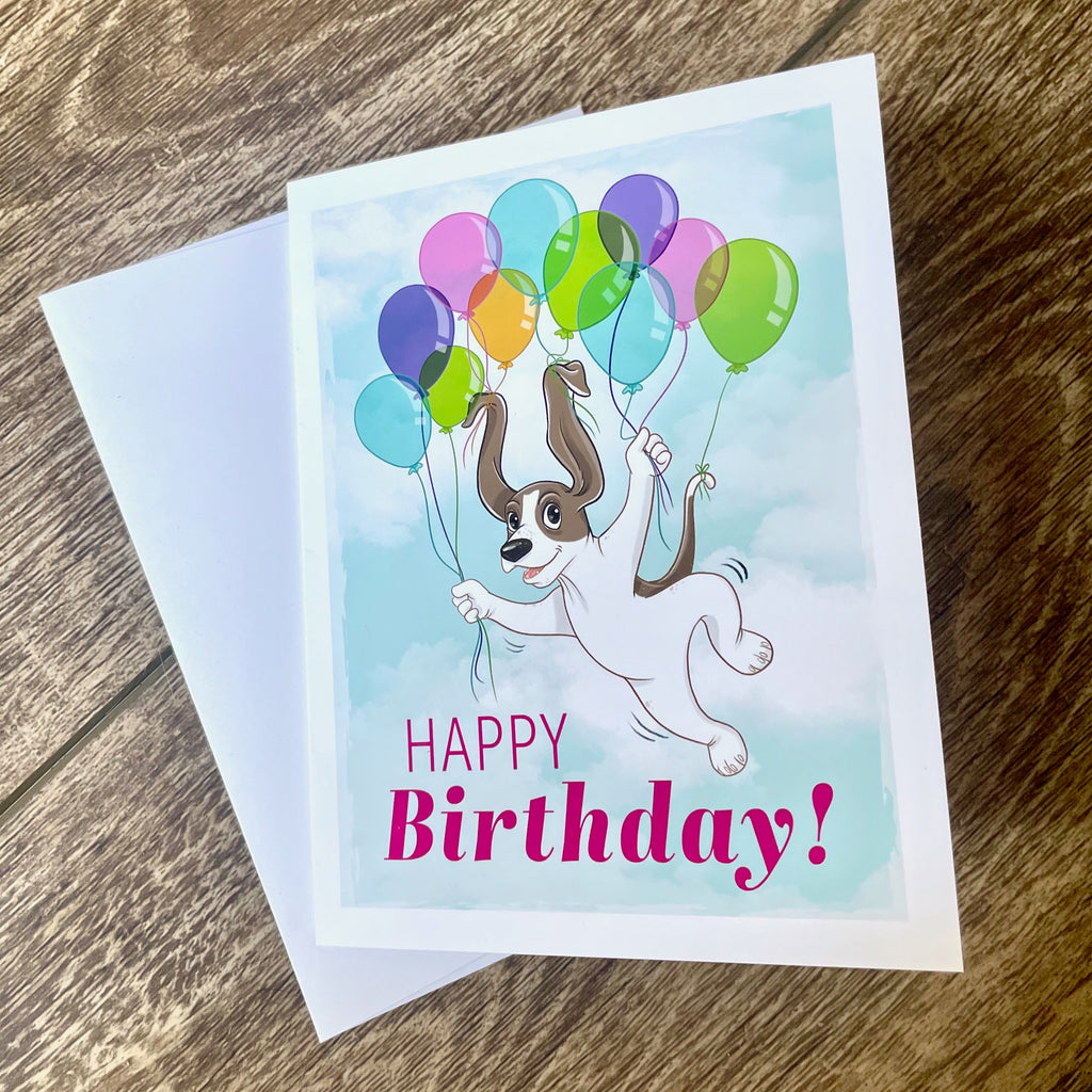 Birthday card with a dog and balloons on a wooden surface.