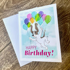 Birthday card with a dog and balloons on a wooden surface.