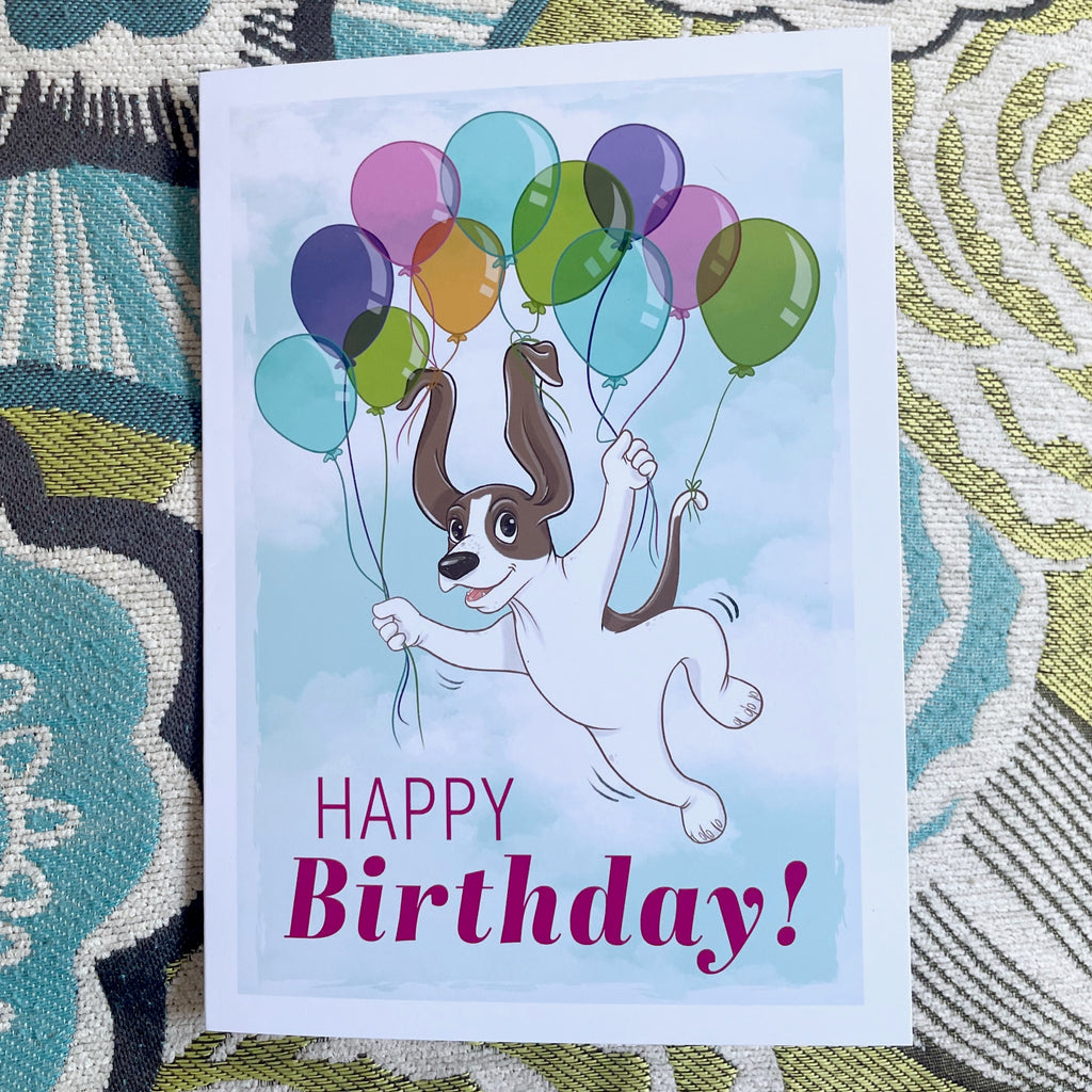Birthday card with a dog holding balloons on a patterned fabric background.