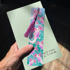 Colorful bookmark with tassel held over a book by a hand