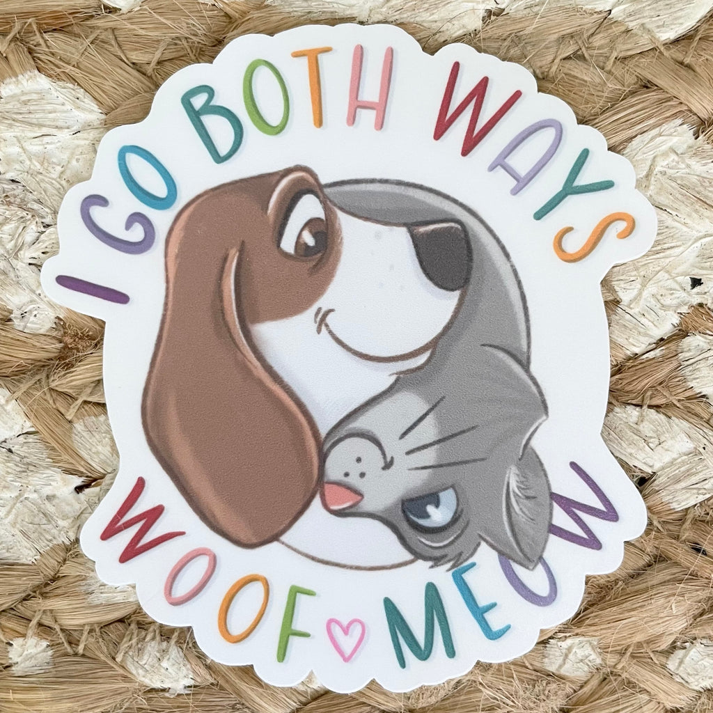 Sticker with cartoon dog and cat faces and text 'I go both ways, woof meow' on a woven background
