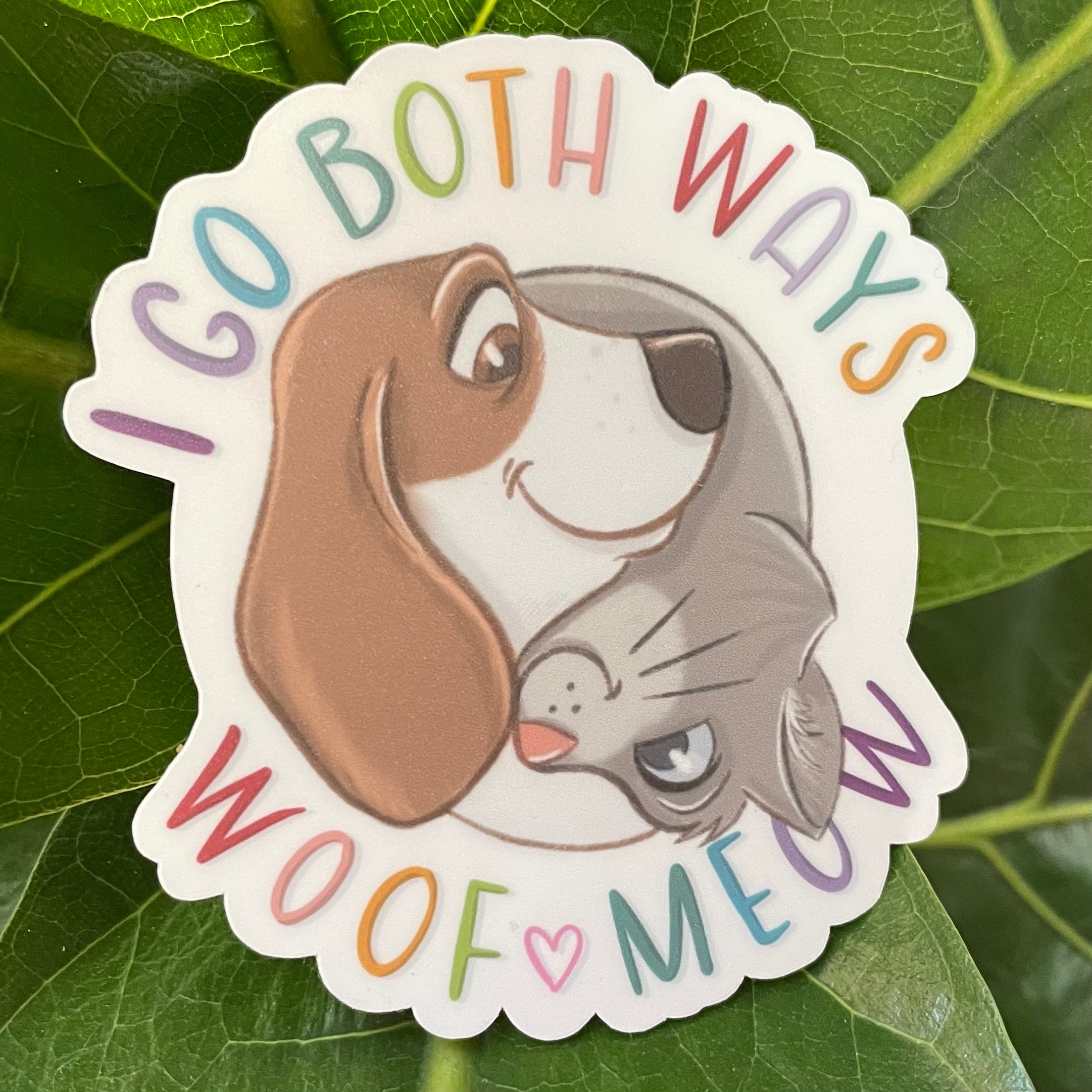 Sticker with a dog and cat hugging with text 'I go both ways, woof meow' on a leaf background