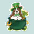 Artwork of a basset hound wearing  green top hat and holding a shamrock sitting in a pot of gold.