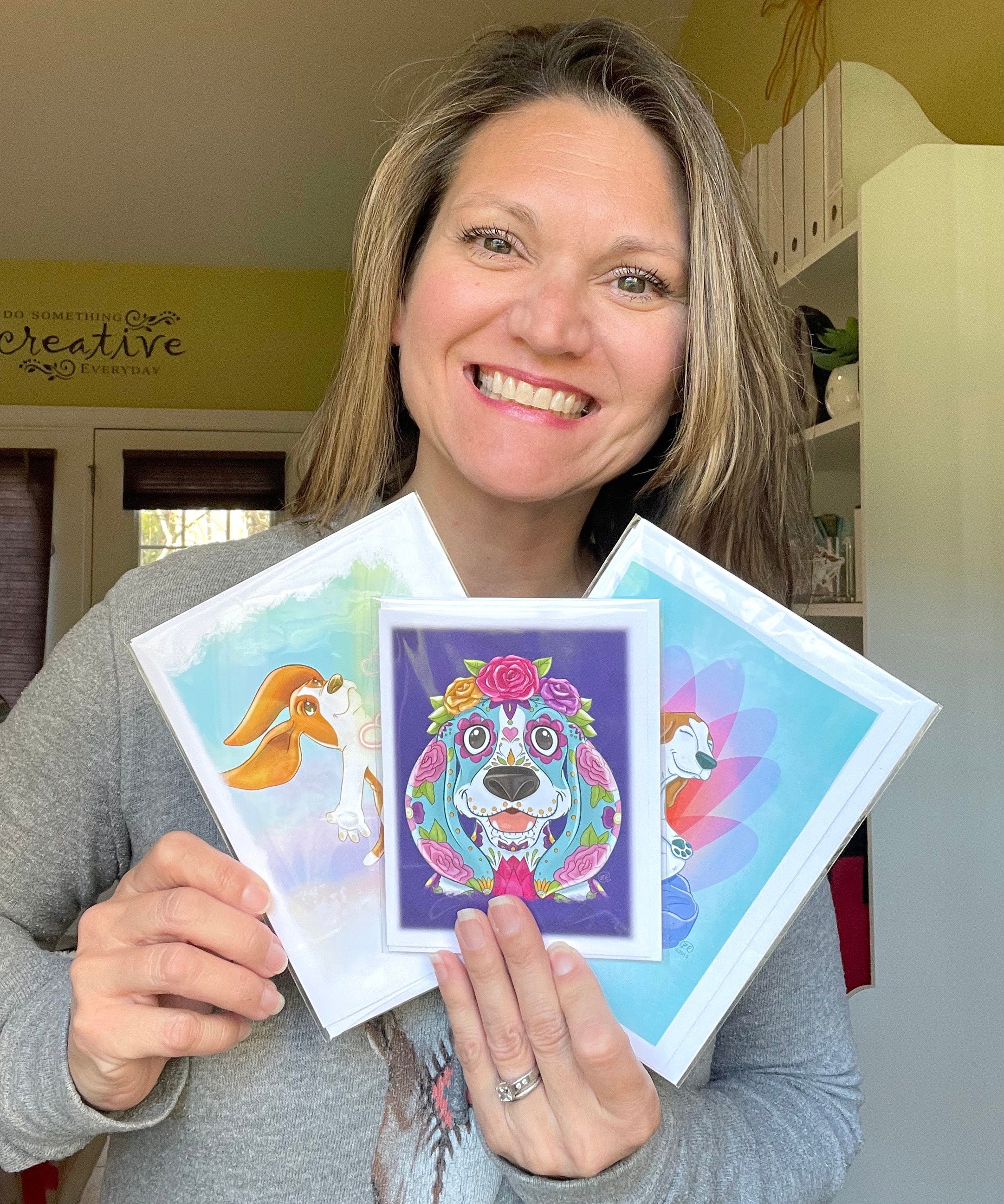 Illustrator Zoe Ranucci holding several basset hound greeting cards that she created.