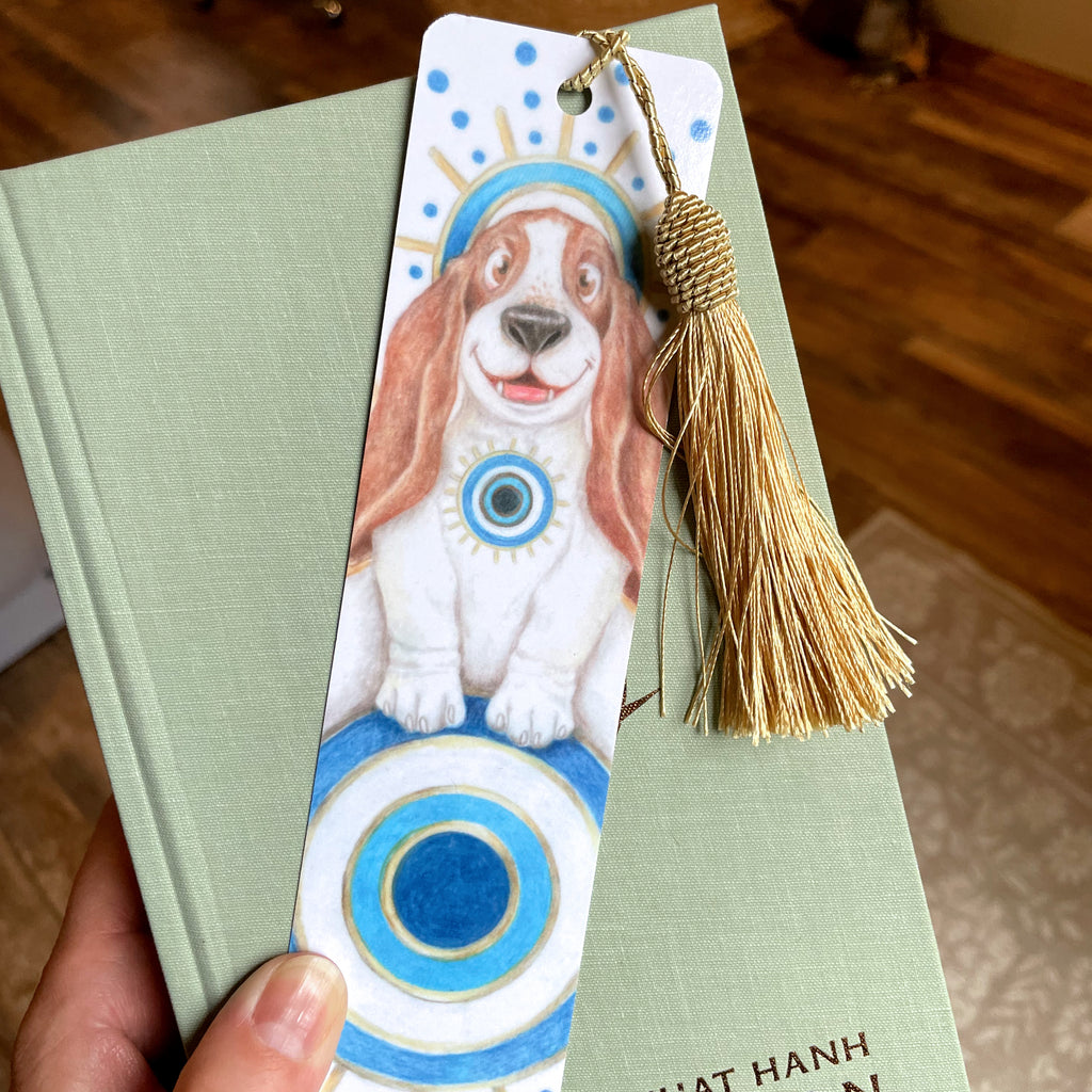 Bookmark with a dog illustration and tassel held over a book. ©Good Dharma Design by Zoe Ranucci